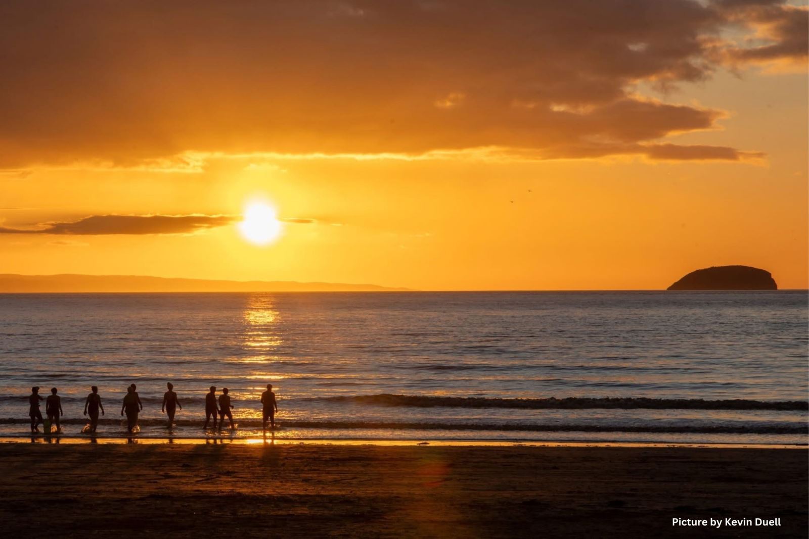 A group of people entering the sea at sunset in Weston-super-Mare